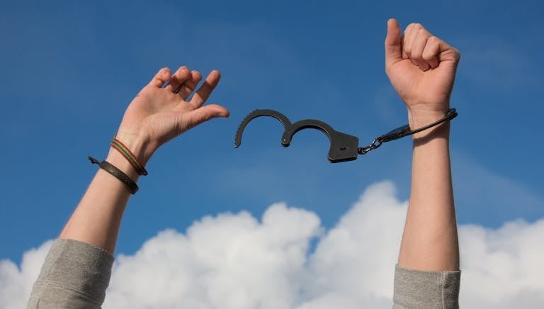 Symbolic image of freedom with open handcuffs against a bright blue sky.