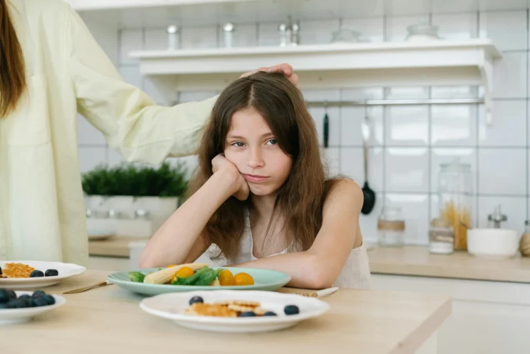 Jeune fille brune semblant attristée devant son assiette. Évoque un problème possible lié à l'alimentation (hpi, tca)